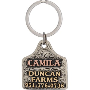 A custom dog tag with personalized engraved bronze lettering built on a silver cow tag-shaped base, western designed 